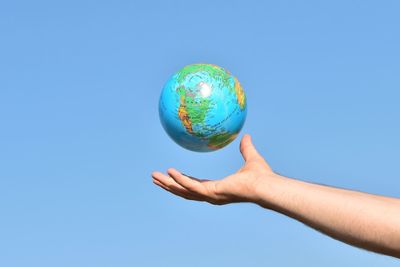 Cropped hand of man reaching globe against clear blue sky