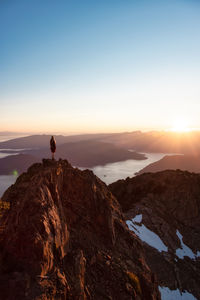 Man standing on rock against sky during sunset