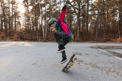 Side view of talented teenage skater jumping with skateboard in park in autumn