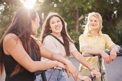 Young female friends spending time together outdoors riding electric scooters