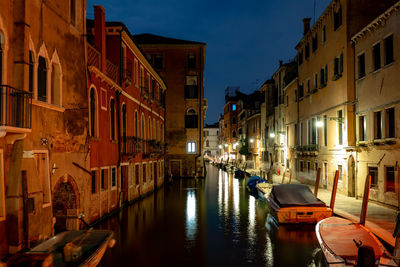 Boats moored on canal amidst buildings in city at night