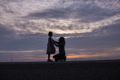 Silhouette woman with girl against sky during sunset