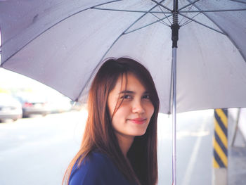 Portrait of smiling woman standing with umbrella on road