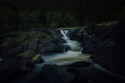 Scenic view of waterfall in forest against sky at night