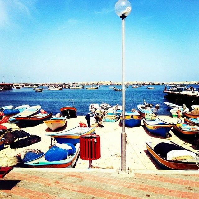 transportation, nautical vessel, mode of transport, moored, boat, sea, water, sky, blue, clear sky, harbor, travel, sunlight, beach, in a row, street light, mast, day, outdoors, incidental people