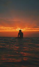 Silhouette of man in sea against sunset sky