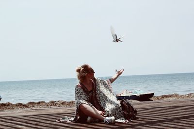 Woman sitting on beach  against clear sky