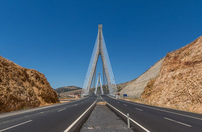 Road by bridge against clear blue sky