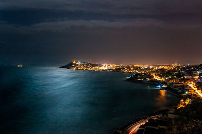 Illuminated city by sea against sky at night