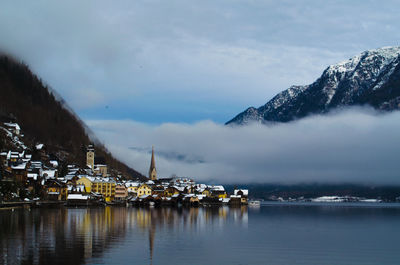 Town by lake and mountain against cloudy sky