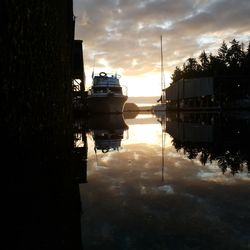 Canal amidst silhouette buildings against sky during sunset