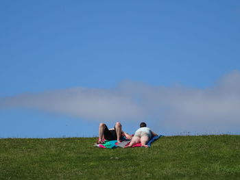 Man and woman relaxing on grassy field against sky
