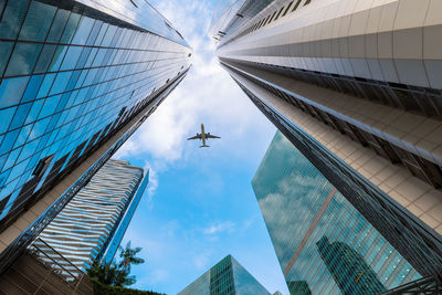 Low angle view of airplane flying over modern buildings against sky