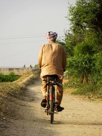 Rear view of man riding bicycle on dirt road