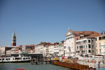 Buildings by river against clear blue sky