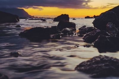 Rocks on beach against sky during sunset