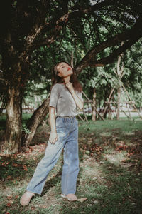 Portrait of woman standing by tree on field