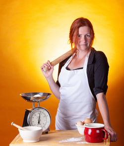 Portrait of woman preparing food standing by orange background