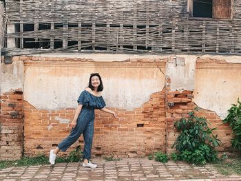 Portrait of young woman standing against brick wall