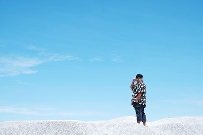 Man standing on sand against blue sky