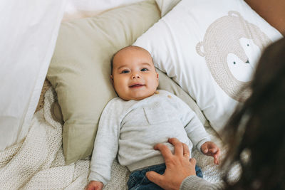 Cute smiling baby boy in beige 5-6 month looking at camera with mother on bed with knitted blanket