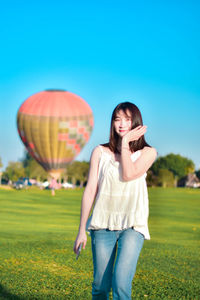 Young woman with balloons on field against clear blue sky