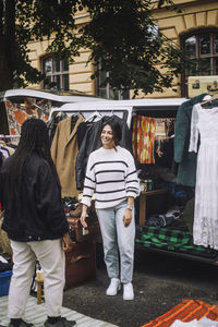 Smiling female owner welcoming customer during during second hand sale at flea market