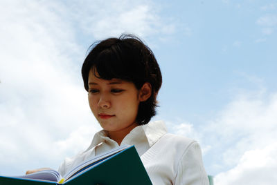 Low angle view of woman reading diary against sky