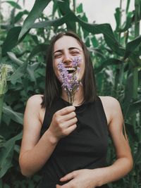 Portrait of young woman holding flowering plant while standing outdoors