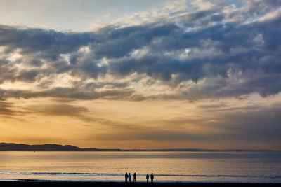 Silhouette people on beach against sky during sunrise