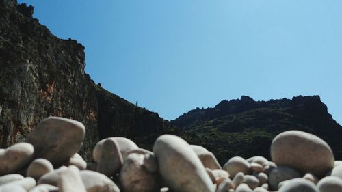 View of rocky beach in front of mountains against clear sky