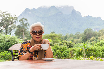 Asin grey white hair senior woman drinking coffee in cafe outdoor with mountain view