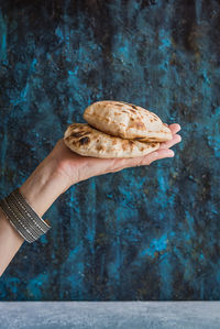 Cropped hand of woman holding flatbread against wall