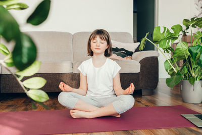 The girl sits in the lotus position and meditates at home in the living room. yoga poses for kids