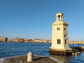 Lighthouse on building by sea against clear blue sky