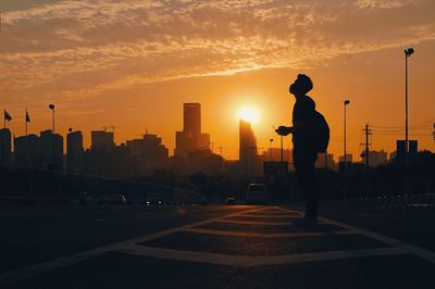 Silhouette man standing on road against sky during sunset