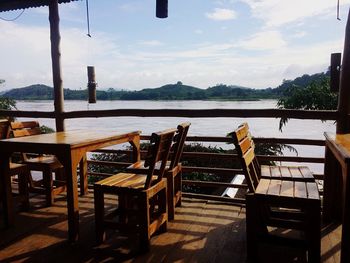 Empty chairs and table by sea against sky