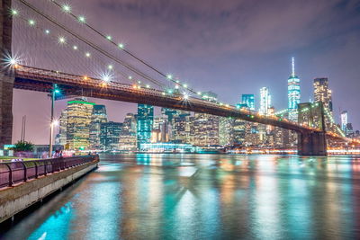 Illuminated bridge over river with buildings in background