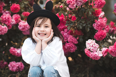 Laugh child girl 4-5 year old wear stylish summer cloth and hat posing in pink roses at background