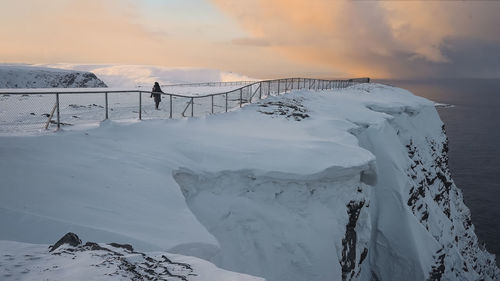 Snow covered land against sky during sunset