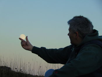 Optical illusion on man holding moon at dusk