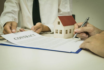 Midsection of real estate agent holding document while client signing on table