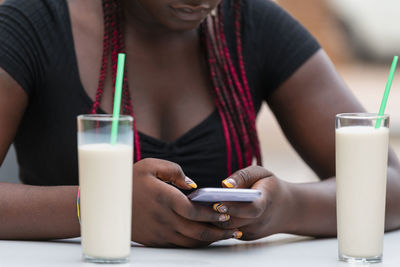 Cropped image of an african woman using her phone with milkshakes on the table in a outdoor cafe