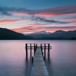 Wooden pier in lake against sky during sunset