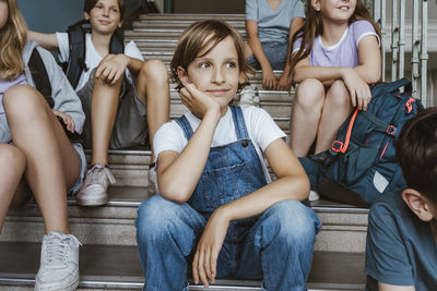 Thoughtful girl leaning on elbow while sitting on staircase with friends in school