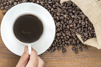 Directly above shot of hand with coffee cup and beans on table