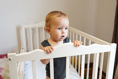 Cute baby girl standing in crib at home