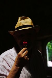 Portrait of man holding hat against black background