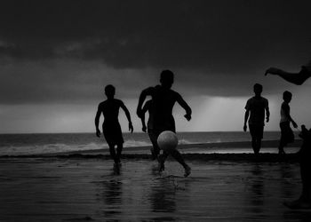 Silhouette children playing on beach against sky