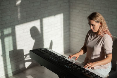 Young woman playing piano against wall